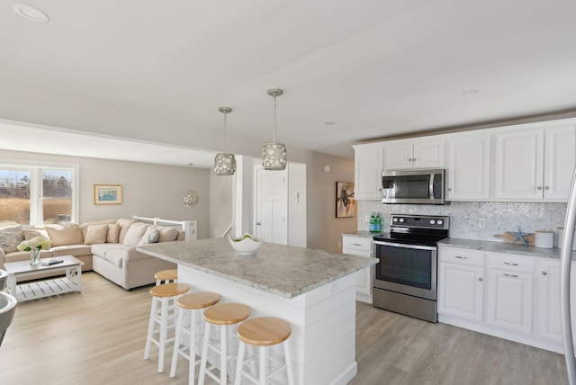 kitchen with a center island, tasteful backsplash, light wood-type flooring, stainless steel appliances, and white cabinetry