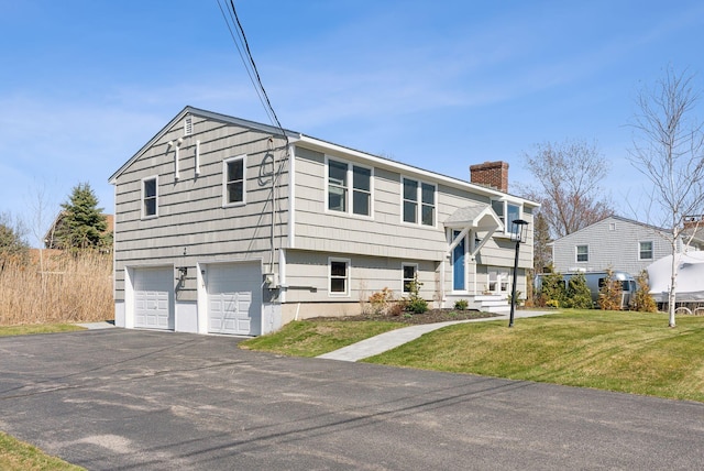 raised ranch with an attached garage, driveway, a chimney, and a front yard