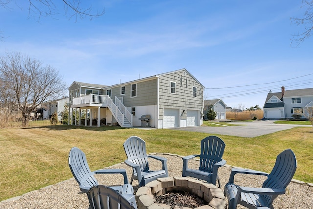 rear view of property featuring a lawn, aphalt driveway, an attached garage, a fire pit, and stairs