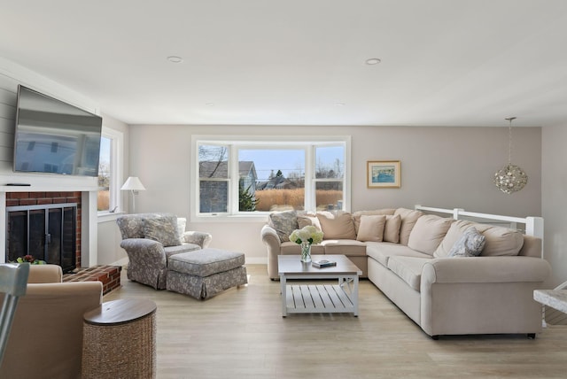 living area with a healthy amount of sunlight, a fireplace, light wood finished floors, and a notable chandelier