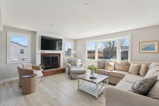 living area with light wood-style floors, a brick fireplace, and a wealth of natural light