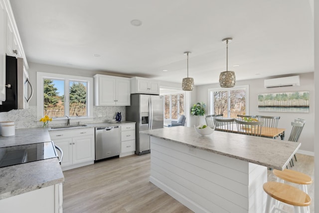 kitchen with plenty of natural light, appliances with stainless steel finishes, tasteful backsplash, a wall mounted air conditioner, and a sink