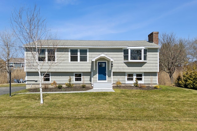 bi-level home featuring entry steps, roof with shingles, a chimney, and a front lawn