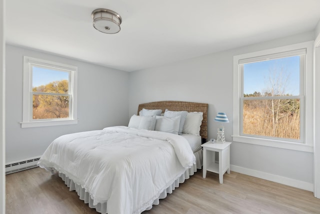 bedroom featuring baseboards, light wood finished floors, and a baseboard heating unit