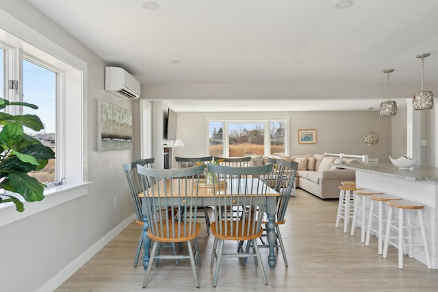 dining room with light wood-style floors, a wall mounted air conditioner, baseboards, and a healthy amount of sunlight