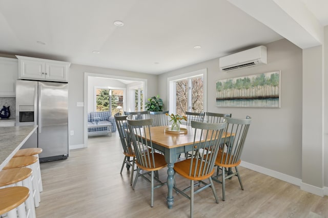dining area with baseboards, light wood finished floors, and a wall unit AC