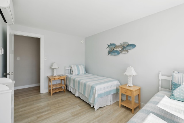 bedroom with baseboards, a wall mounted AC, and light wood-type flooring