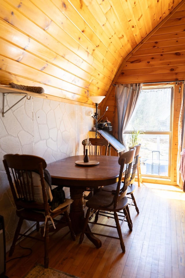 dining space featuring hardwood / wood-style floors, vaulted ceiling, wooden ceiling, and wood walls