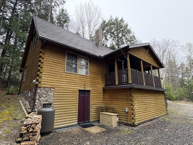 view of front of home with a balcony, log exterior, a chimney, and metal roof