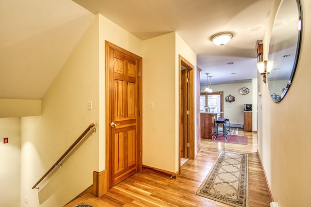 hallway with an upstairs landing, light wood-style floors, and baseboards