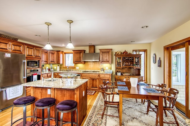 kitchen featuring light stone countertops, brown cabinets, light wood-type flooring, a kitchen island, and appliances with stainless steel finishes