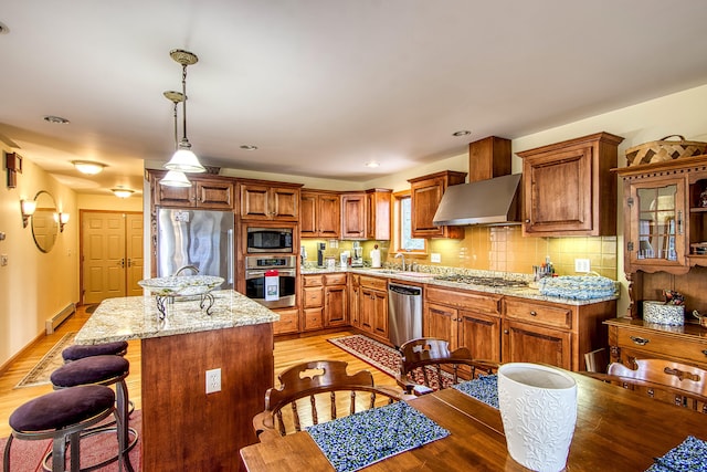 kitchen featuring range hood, a sink, a kitchen island, appliances with stainless steel finishes, and a baseboard radiator