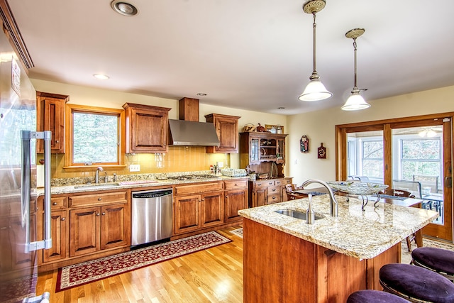 kitchen with plenty of natural light, wall chimney exhaust hood, dishwasher, and a sink