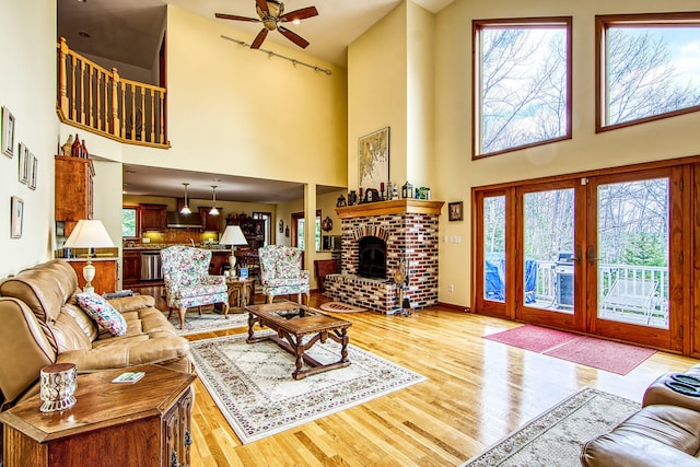 living area with a brick fireplace, ceiling fan, light wood-style flooring, and a high ceiling