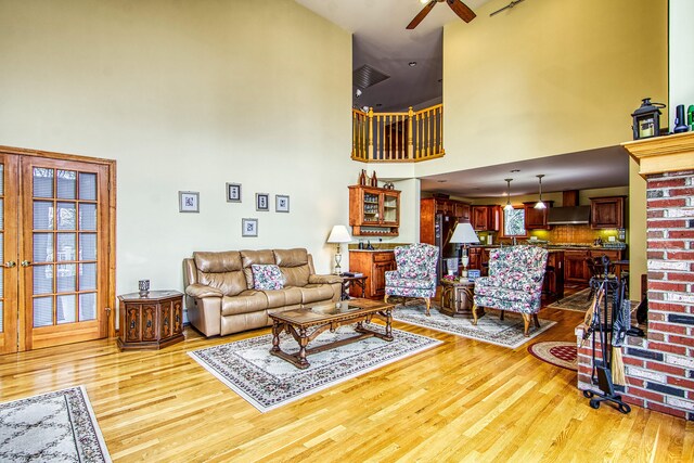 living room with a healthy amount of sunlight, ceiling fan, light wood finished floors, and a towering ceiling