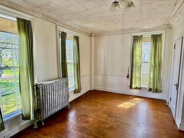 unfurnished room featuring radiator, hardwood / wood-style flooring, ornamental molding, and baseboards