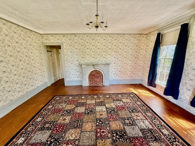 unfurnished living room with a chandelier, wood finished floors, crown molding, a fireplace with flush hearth, and baseboards