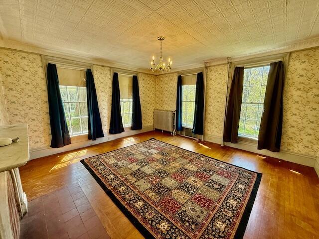spare room featuring radiator heating unit, a chandelier, hardwood / wood-style floors, wallpapered walls, and crown molding