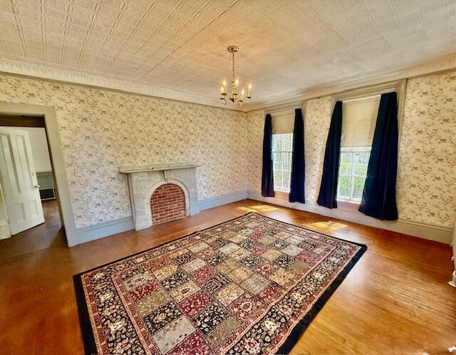 unfurnished living room with wood finished floors, a chandelier, crown molding, a fireplace with flush hearth, and baseboards