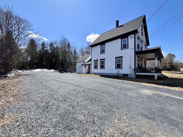 view of side of property featuring a chimney, gravel driveway, roof with shingles, and covered porch