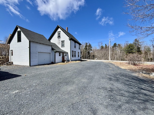 exterior space with gravel driveway, a chimney, and a garage