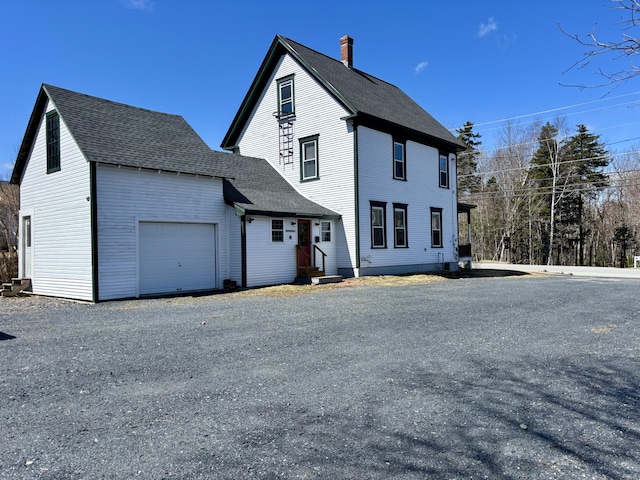exterior space with an attached garage, a shingled roof, and a chimney