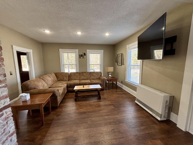 living area with heating unit, baseboards, a textured ceiling, and dark wood-type flooring