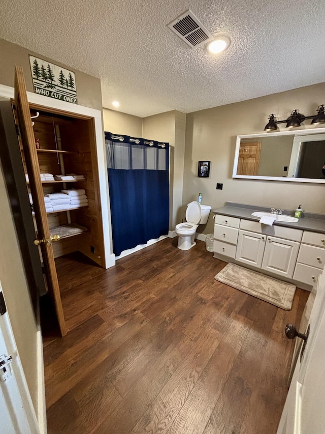 full bath with a shower with curtain, a textured ceiling, visible vents, wood finished floors, and vanity