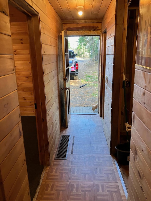 doorway with wooden walls, tile patterned floors, visible vents, and wood ceiling