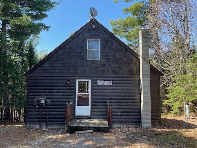 rear view of property with log veneer siding, a chimney, and an outdoor structure