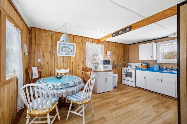 kitchen featuring white cabinets, light wood finished floors, wood walls, and white appliances