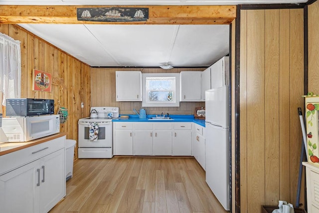 kitchen featuring wooden walls, a sink, white appliances, light wood-style floors, and white cabinetry