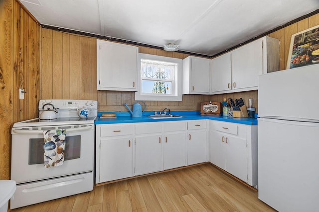 kitchen with white cabinets, light wood-style flooring, a sink, white appliances, and wooden walls