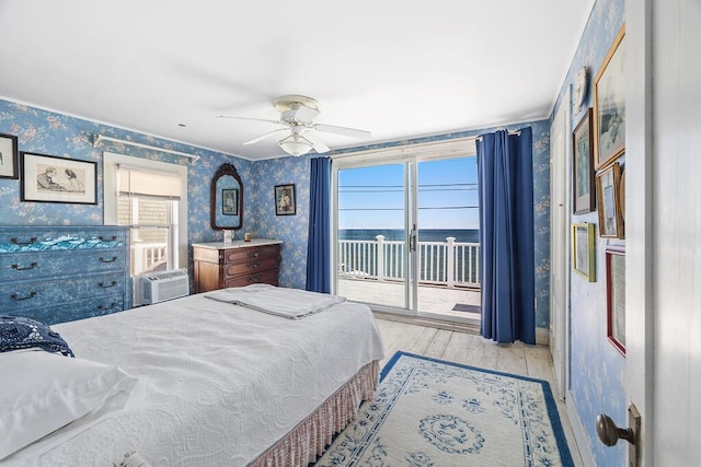 bedroom with wallpapered walls, a water view, a ceiling fan, hardwood / wood-style flooring, and access to outside