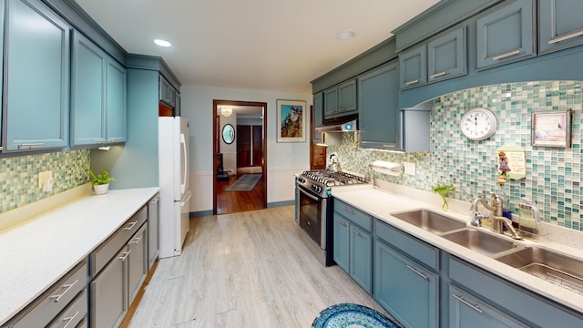 kitchen featuring stainless steel range with gas stovetop, light wood-type flooring, freestanding refrigerator, under cabinet range hood, and a wainscoted wall