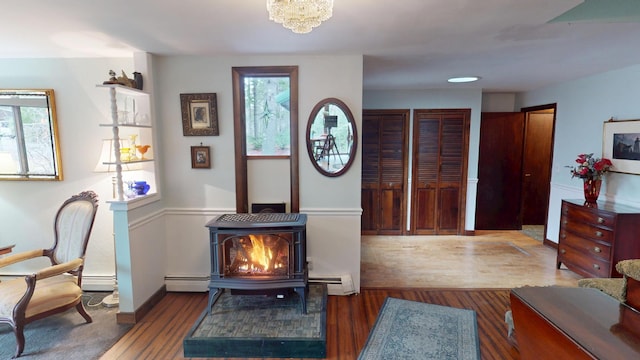 sitting room featuring a baseboard radiator, a wood stove, plenty of natural light, and wood finished floors