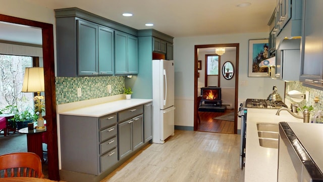 kitchen with freestanding refrigerator, tasteful backsplash, light wood-type flooring, gas stove, and light countertops