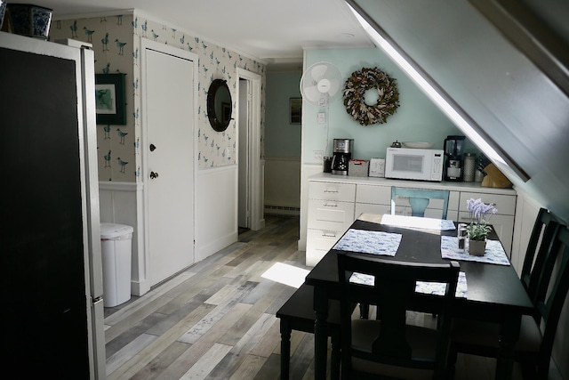 dining area with light wood-style flooring, baseboard heating, wainscoting, and wallpapered walls