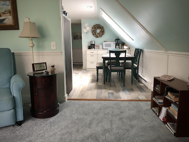 dining room with wainscoting, baseboard heating, light wood-type flooring, and lofted ceiling with skylight