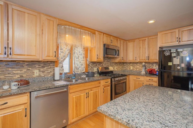 kitchen featuring light wood-style flooring, a sink, dark stone counters, stainless steel appliances, and decorative backsplash