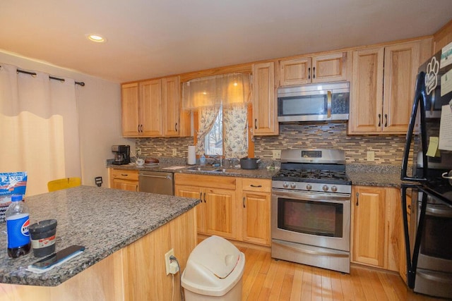 kitchen featuring tasteful backsplash, dark stone countertops, a sink, stainless steel appliances, and light wood-style flooring