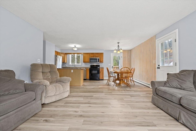 living area with baseboard heating, an inviting chandelier, light wood-style floors, and a textured ceiling