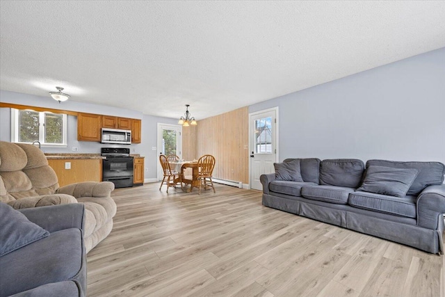 living area featuring a notable chandelier, light wood-type flooring, a textured ceiling, and a healthy amount of sunlight