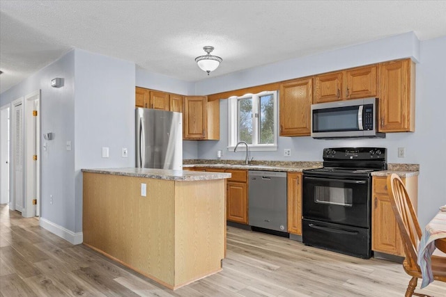 kitchen with light wood-type flooring, appliances with stainless steel finishes, light countertops, and a textured ceiling