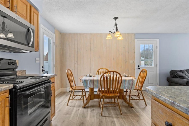 dining space featuring wood walls, light wood-style flooring, a chandelier, and a textured ceiling