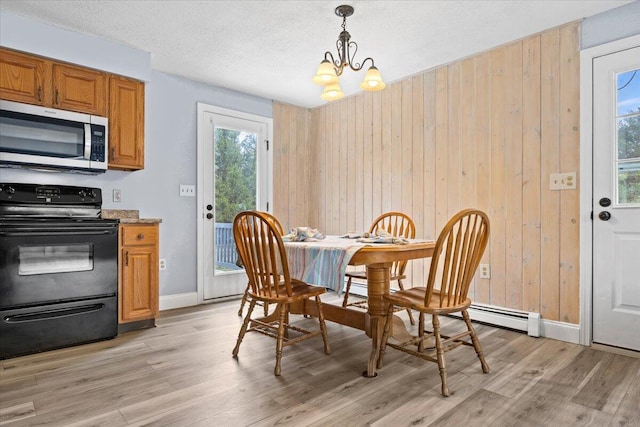 dining space featuring light wood-style flooring, a textured ceiling, an inviting chandelier, and wooden walls