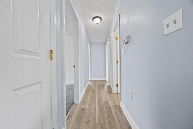 hall with light wood-type flooring, a textured ceiling, and baseboards