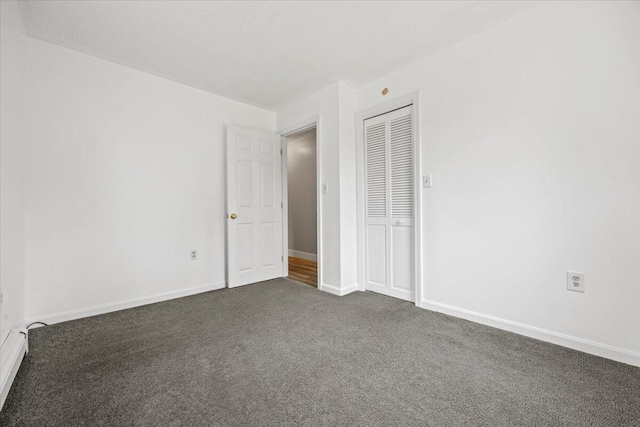 unfurnished bedroom with dark carpet, baseboards, a closet, and baseboard heating