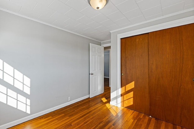 unfurnished bedroom featuring a closet, wood-type flooring, baseboards, and crown molding