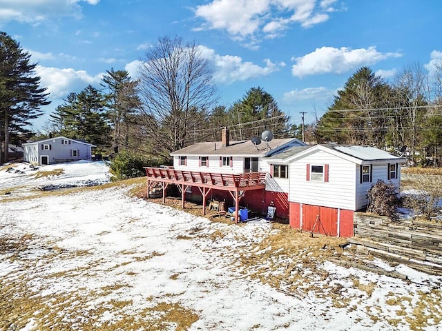 snow covered house featuring a chimney and a wooden deck